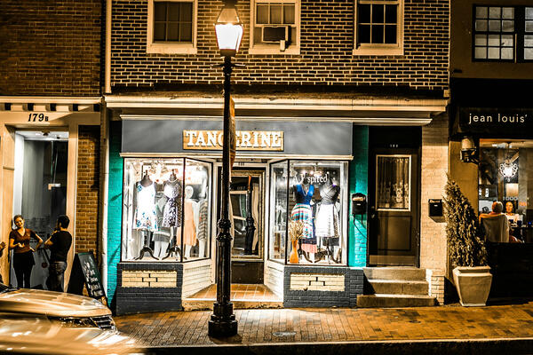 Picture of a downtown main street with shops, street lamp, and passing cars.